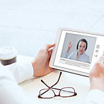 Man looking at the screen of a tablet where there is a woman wearing a headseat.