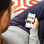 Paris: Man holding using the Tripadvisor hotel booking app on the new Apple iPhone X 10 Display while seating in couch with Retina Display screen featuring all home apps