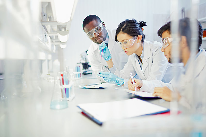 Three scientists wearing eye protection glasses study a new substance in a laboratory.