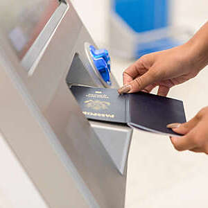 An unrecognizable woman stands in front of an airport kiosk and holds her passport open to scan it.