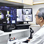 Mature radiologist analyzing MRI scan on computer monitors. Male doctor is sitting at desk in office. He is working at hospital.